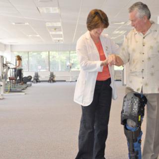 A healthcare professional assists a patient in physical therapy, with a focus on using a prosthetic leg.