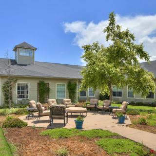 A charming house with a well-maintained garden featuring outdoor seating and a patio on a sunny day.