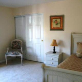 A cozy bedroom with a bed, chair, and nightstand featuring a lamp and wall art.