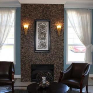 A cozy living room with a stone fireplace, elegant chairs, and soft curtains framing the windows.