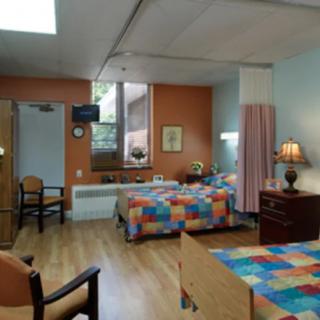 A hospital room with two beds featuring colorful bedspreads, a window, and chairs.