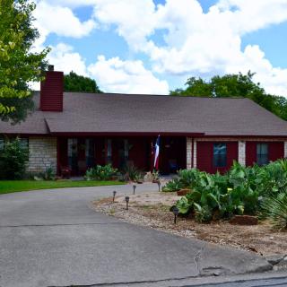 A charming house with a long driveway and vibrant garden under a partly cloudy sky.