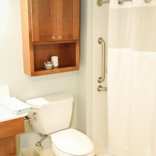 A clean and well-organized bathroom featuring a toilet, shower with a white curtain, and a wooden storage cabinet.