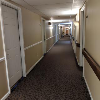 A long indoor hallway with doors on either side and carpeted flooring.