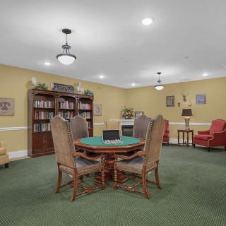 A cozy library interior with a central table surrounded by chairs, bookshelves along the walls, and warm lighting.