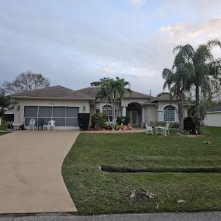 A spacious suburban home with a well-kept front yard and palm trees.