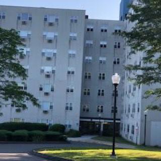 A view of a residential building with numerous windows and surrounding trees in daylight.