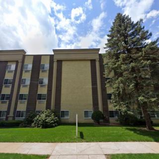 A residential apartment building with trees and a partly cloudy sky.