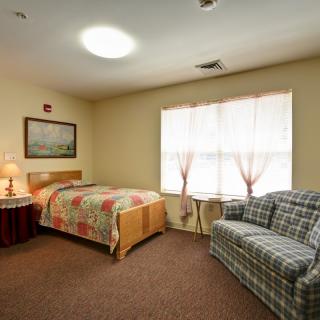 A cozy bedroom with a single bed, sofa, and a large window letting in natural light.