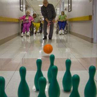 Seniors enjoying a game of indoor bowling in a nursing home corridor.