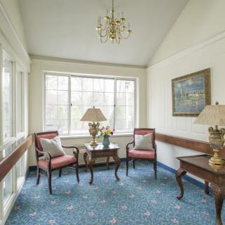 A cozy sitting area featuring two chairs, a small table with lamps, and a large window letting in natural light.