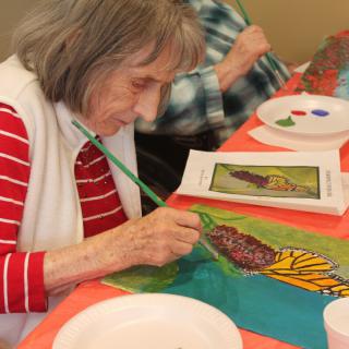 An elderly woman painting a colorful artwork at a table.