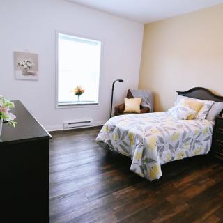 A cozy bedroom with a bed, chair, lamp, and wooden flooring.