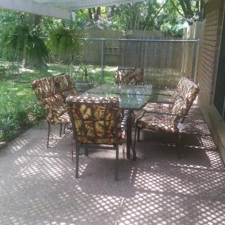 A cozy outdoor patio with a glass table and patterned chairs set in a lush backyard.