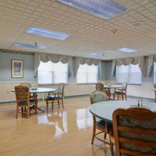 A quiet dining area with several tables and chairs, featuring large windows with curtains.