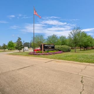 A scenic view of a park entrance featuring a flag and well-maintained greenery under a clear blue sky.