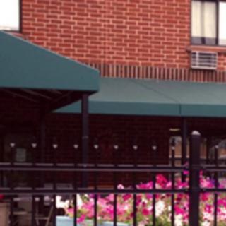 A view of a brick building with an awning, colorful flowers, and a black fence.