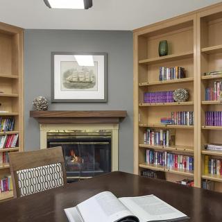 A cozy library room with wooden bookshelves, a fireplace, and an open book on the table.
