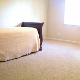A minimalist bedroom with a bed, carpeted floor, and a window.