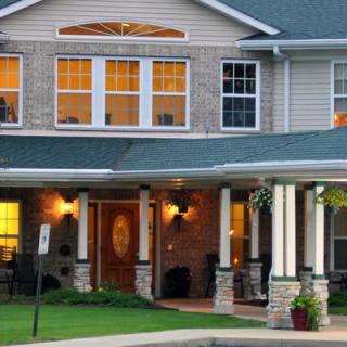 A cozy house with a lit porch and large windows during the evening.