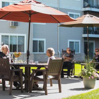 People sitting and conversing on a sunny patio with umbrellas.
