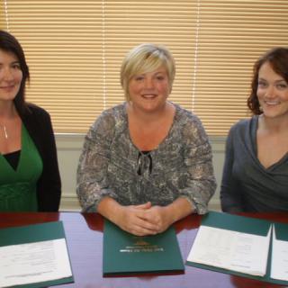 Three women sitting at a table with documents in an office setting.