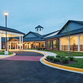 A well-lit building entrance with a landscaped driveway during the evening.