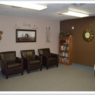A cozy waiting room with leather chairs, a bookshelf, wall art, and a decorative clock.