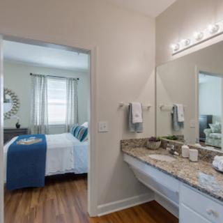A modern bathroom with a granite countertop and wood flooring, connected to a cozy bedroom.