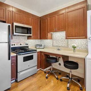 A modern kitchen featuring wooden cabinets, equipped with a stove, microwave, refrigerator, and washer dryer. The counter space includes two chairs for seating.