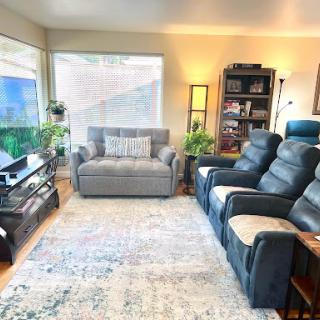 A cozy living room featuring a comfortable sofa, reclining chairs, and plenty of greenery.
