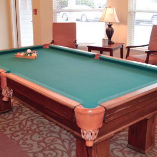 A billiard table set up in a cozy game room with chairs and a lamp.