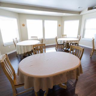 A spacious and well-lit dining area featuring several round tables with chairs, designed for gatherings or meals.