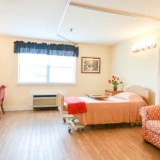 A well-lit hospital room featuring a bed, chair, and a window with curtains.