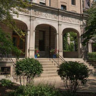 A historic building entrance with columns and greenery.