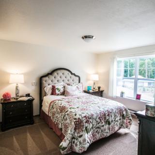 A cozy bedroom with a floral-patterned bedspread, bedside lamps, and a large window letting in natural light.