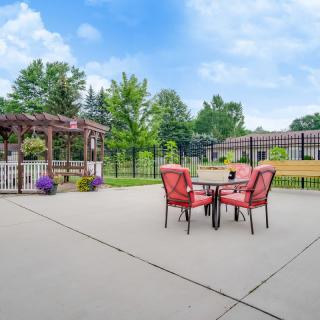 A spacious patio with red outdoor furniture, a pergola, and landscaped surroundings.