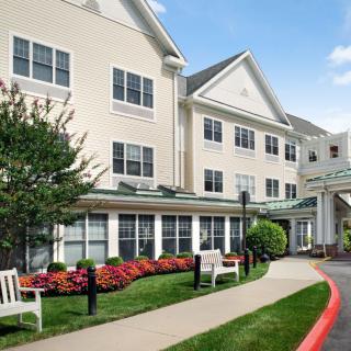 A large residential building with a landscaped garden and benches in the foreground.