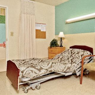 A well-lit hospital room featuring a patient bed and bedside table.
