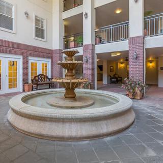 A serene indoor courtyard featuring a central fountain surrounded by benches and plants.