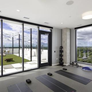 A modern yoga room with large windows offering a stunning city view, equipped with mats and exercise equipment.