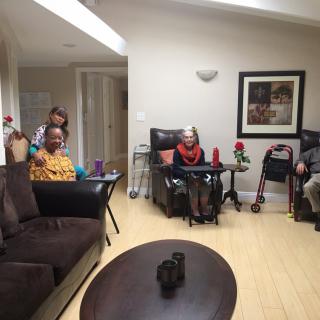 A group of elderly individuals sitting in a living room setting, some with wheelchairs.