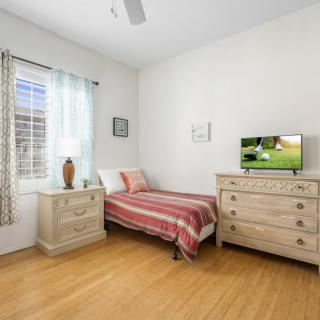 A cozy bedroom featuring a single bed, dresser, and TV with minimalist decor.