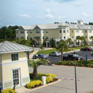 A view of a residential apartment complex with a parking lot and landscaped gardens.