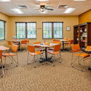 A classroom interior with orange chairs and tables arranged neatly, featuring large windows and a beige color scheme.