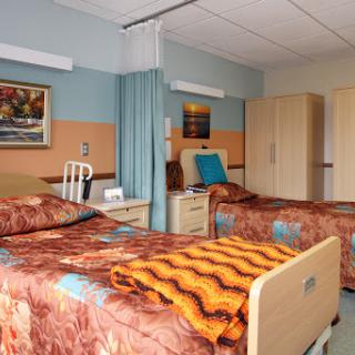 A well-lit hospital patient room featuring two beds with colorful bedding and comfortable furnishings.
