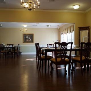 An elegant dining room with wooden tables and chairs, featuring a chandelier and large windows.