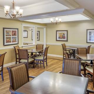 A cozy dining area with several tables and chairs, featuring elegant lighting and wood flooring.