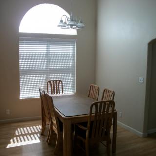 A minimalist dining room with a wooden table and chairs, illuminated by natural light from a large window.