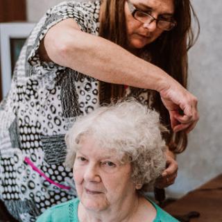 A caregiver styles the hair of an elderly woman in a warm and caring environment.